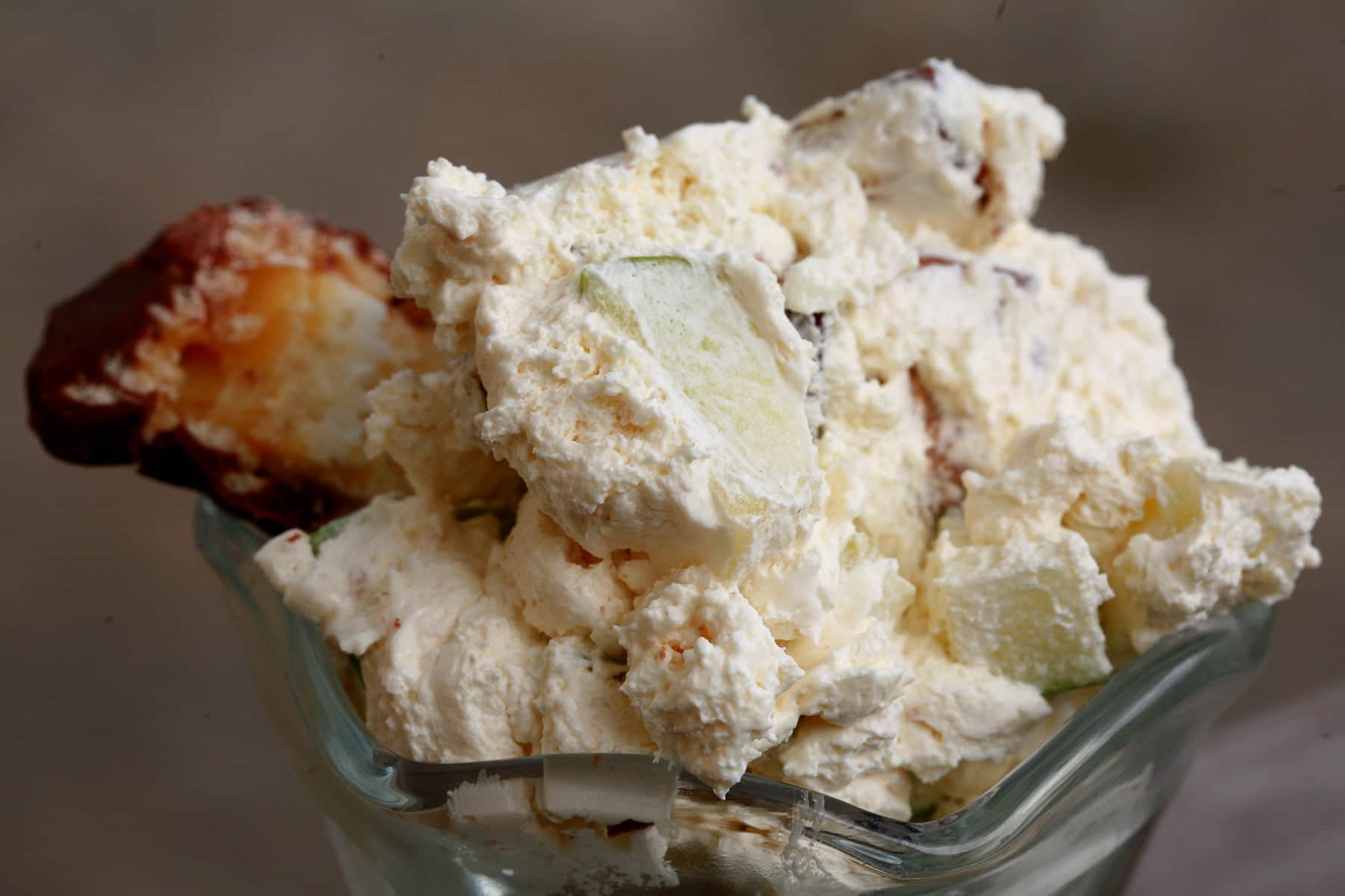 A fluted dessert bowl with Canadian Candy Bar Salad - an off-white, fluffy whipped cream based dessert with chunks of apple and candy bar visible throughout.