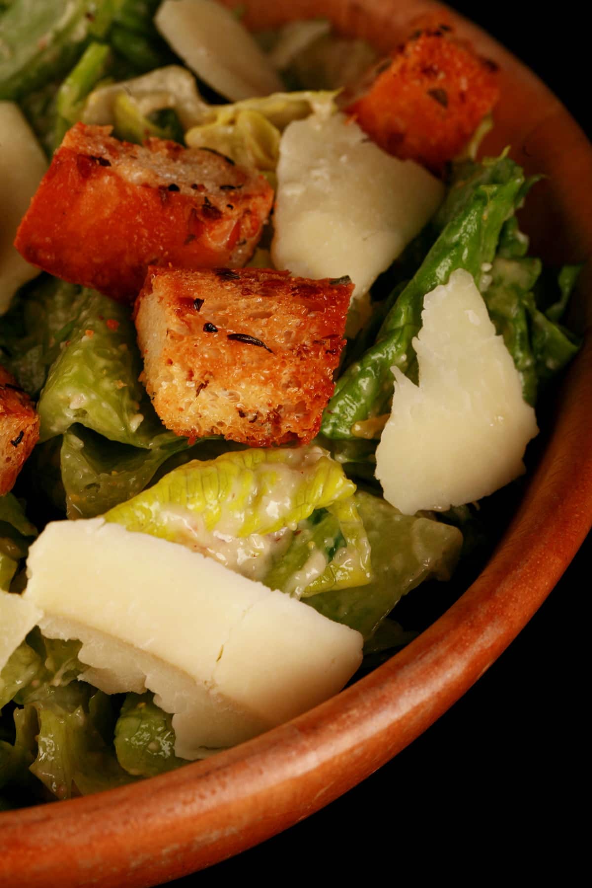 A bowl of "extreme" caesar salad, with big flakes of Parmesan cheese, and croutons.
