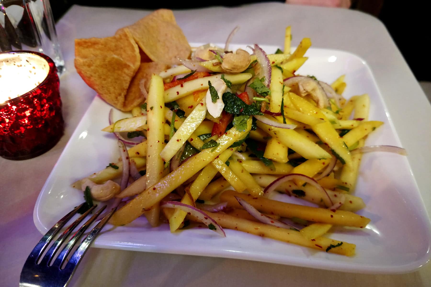 A plate of mango salad, on a restaurant table.