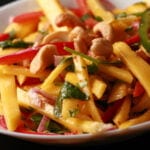 A close up view of Mango Salad - thin sticks of mango, red pepper, green pepper, red onions, and cashews. It's dressed with lime juice and pieces of cilatro and mint.