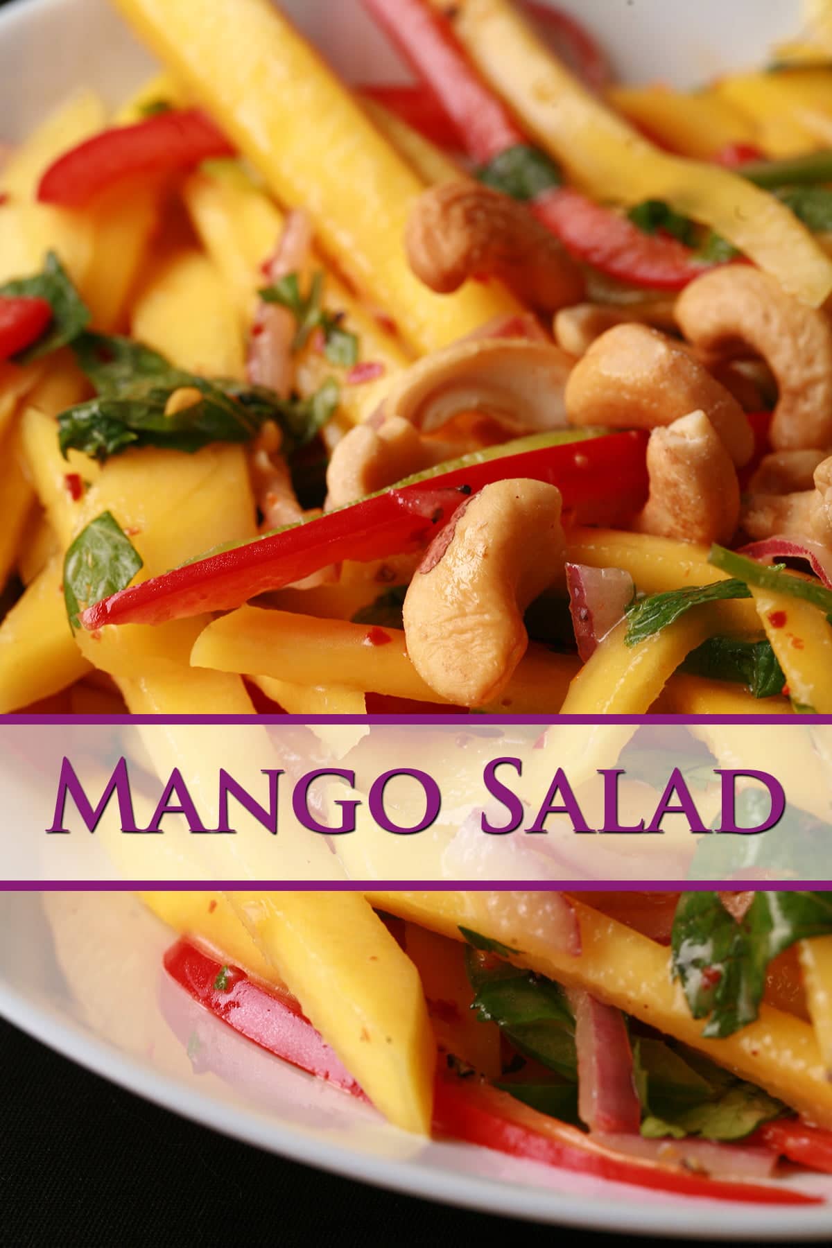 A close up view of Mango Salad - thin sticks of mango, red pepper, green pepper, red onions, and cashews. It's dressed with lime juice and pieces of cilatro and mint.