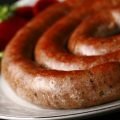 A large coil of sausage on a white plate. It's garnished with slices of beet pickles and some parsley.