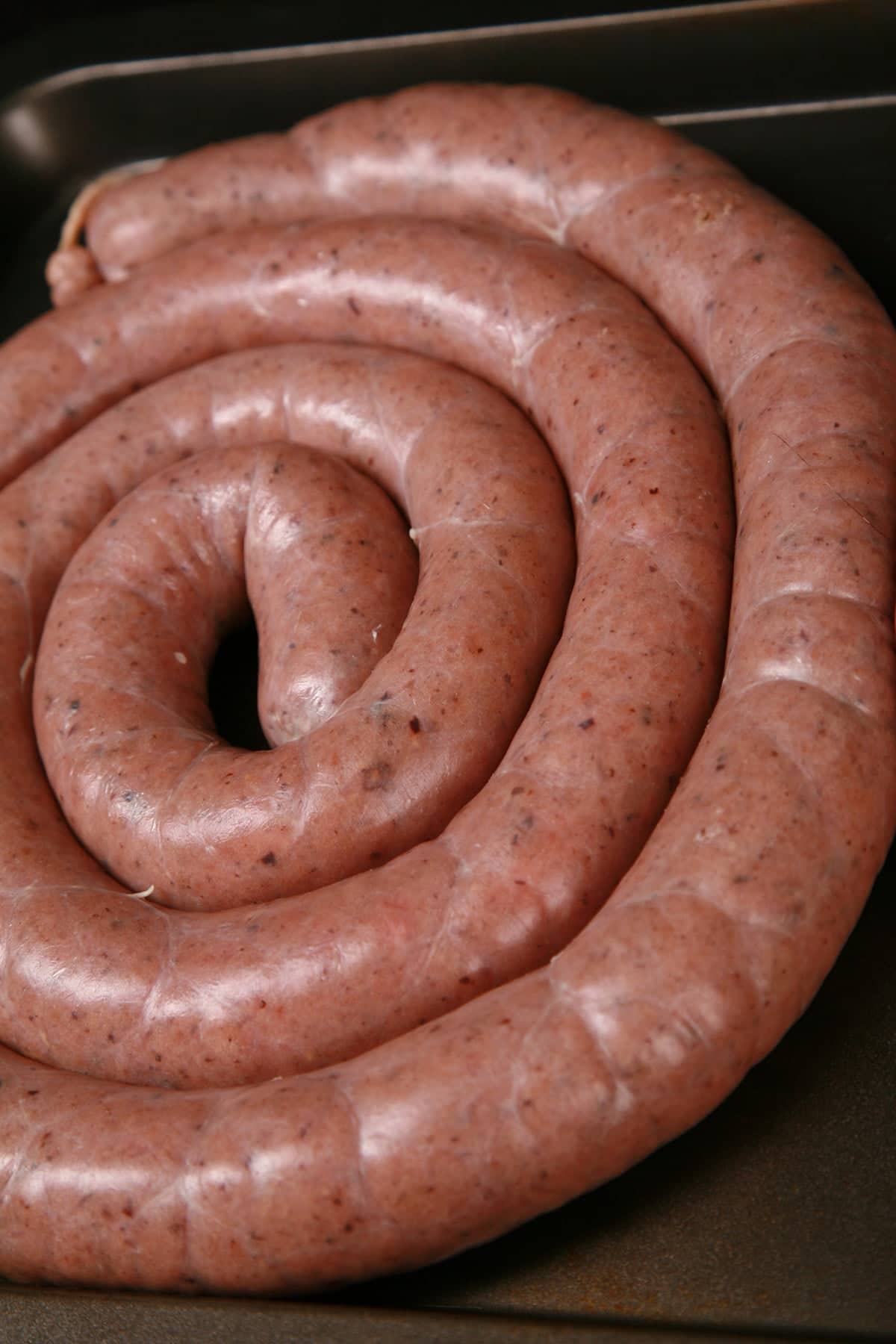 A large coil of Swedish potato sausage on a white plate. It's garnished with slices of beet pickles and some parsley.