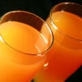 Two glasses of homemade Beep Drink - a orange coloured juice drink - against a black background.