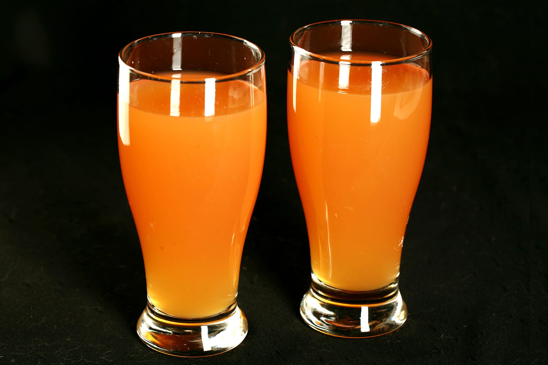 Two glasses of homemade Beep Drink - a orange coloured juice drink - against a black background.