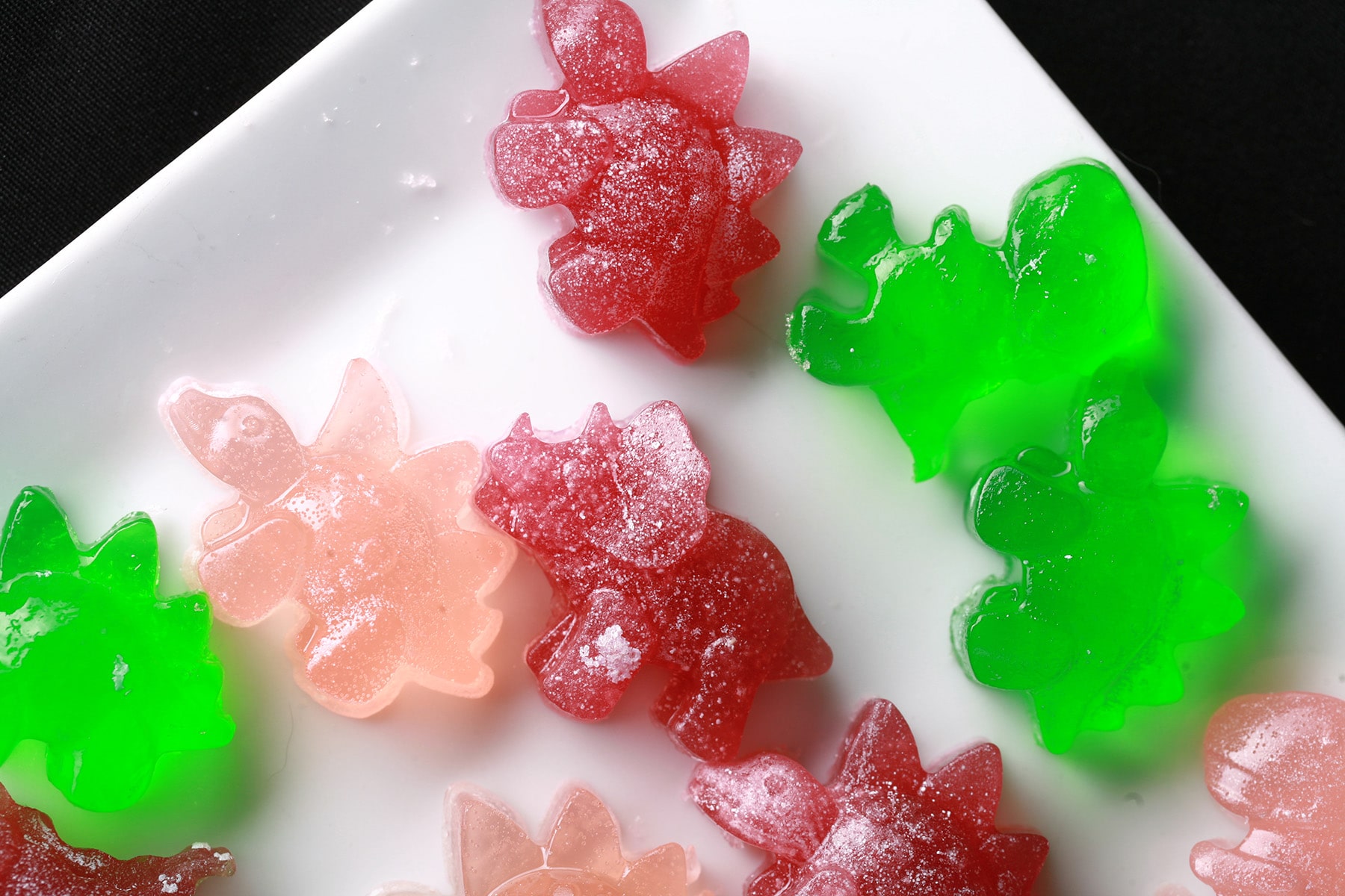 A white plate with homemade BCAA Gummies. They are pink, green, and purple, shaped like dinosaurs.