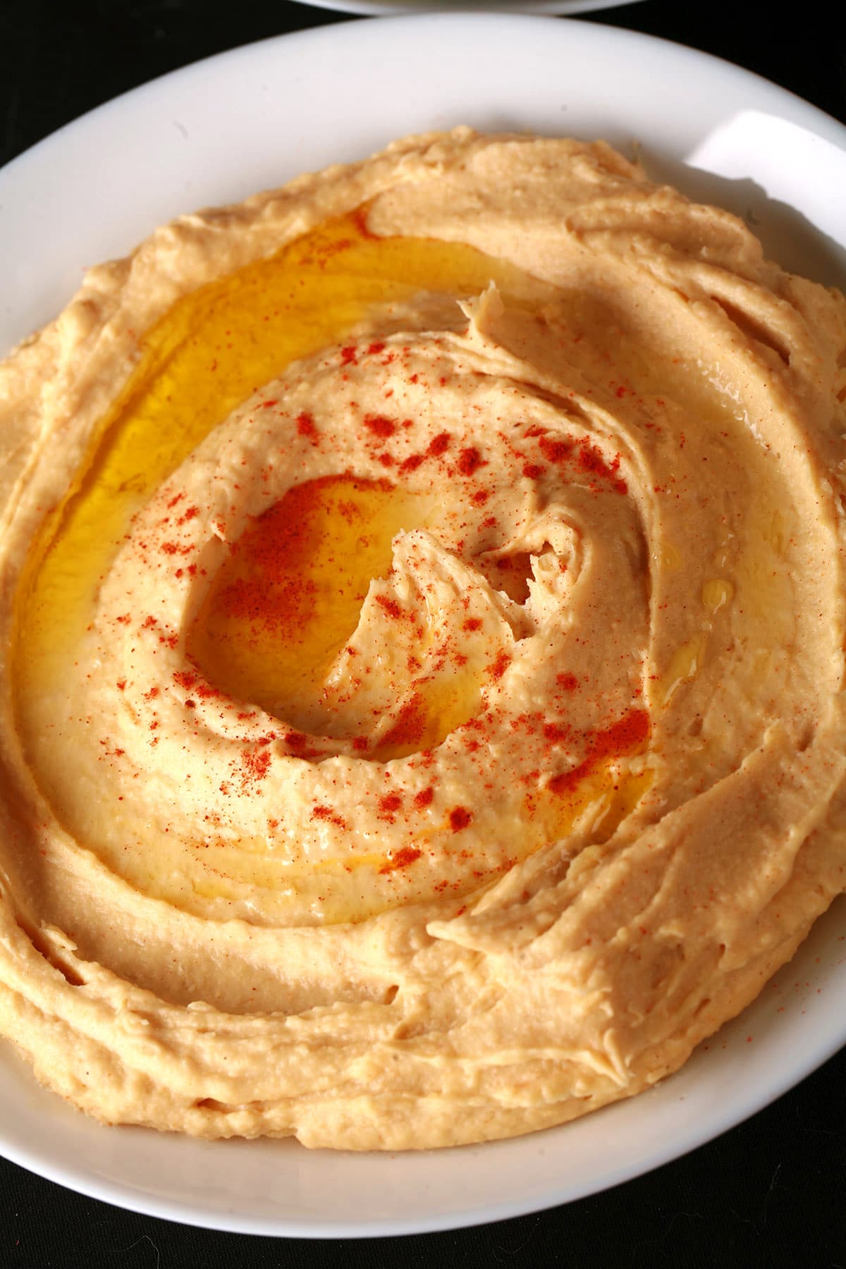A white bowl of smooth hummus.  There is olive oil and a sprinkling of paprika on top.