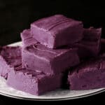 A small white plate stacked with squares of deep purple ube fudge.