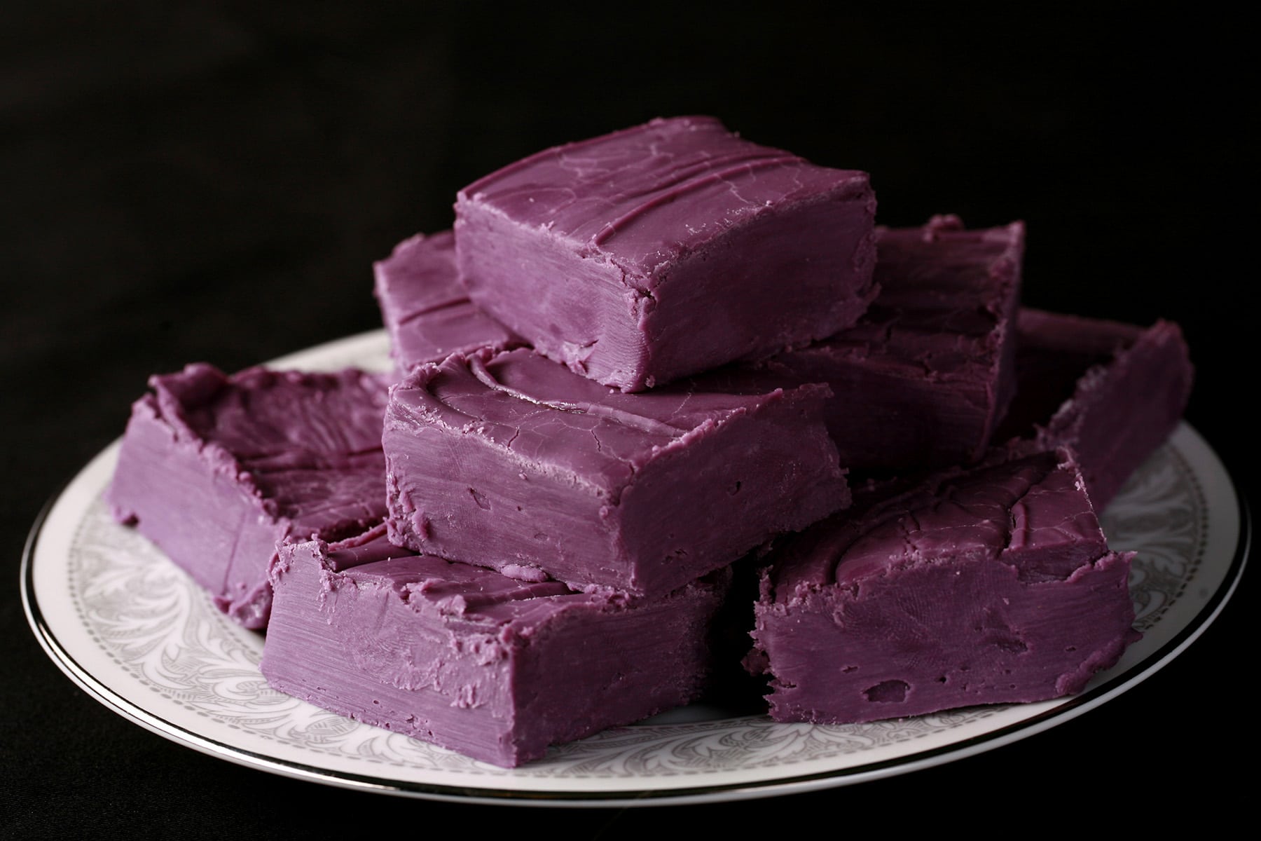 A small white plate stacked with squares of deep purple ube fudge.