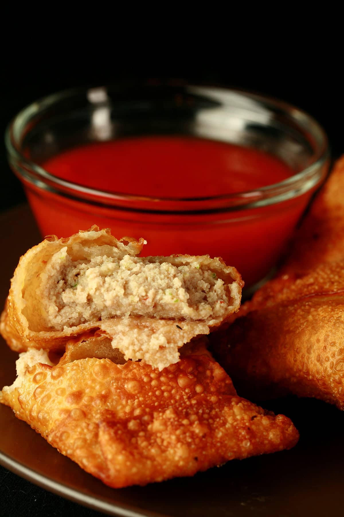 A small round plate holds several halifax style meat paste egg rolls, next to a small bowl of deep orange plum sauce.