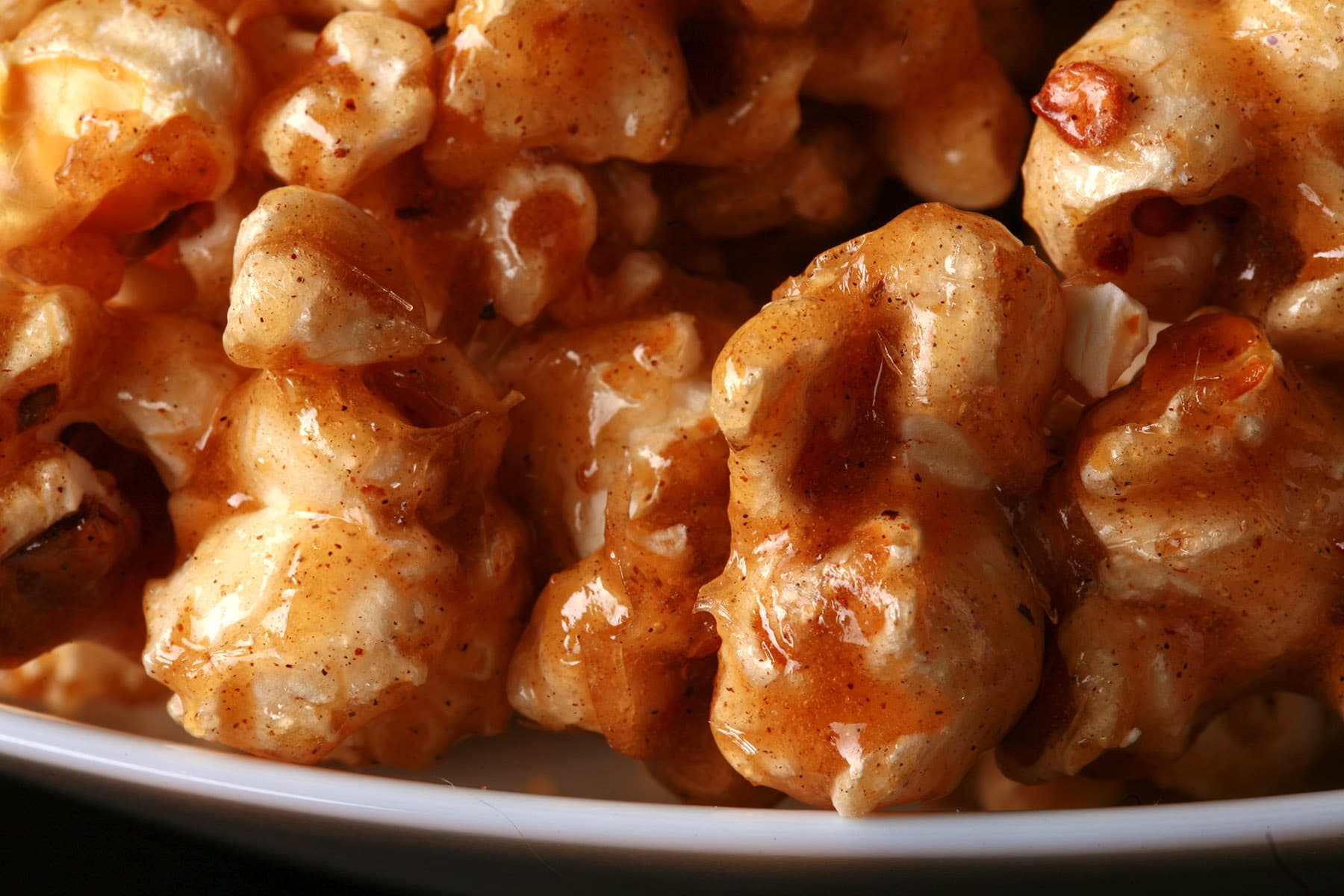 Close up photo of a bowl of caramel popcorn. The caramel has spices visible throughout.