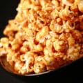 Close up photo of a bowl of caramel popcorn. Spices are visible throughout the caramel.