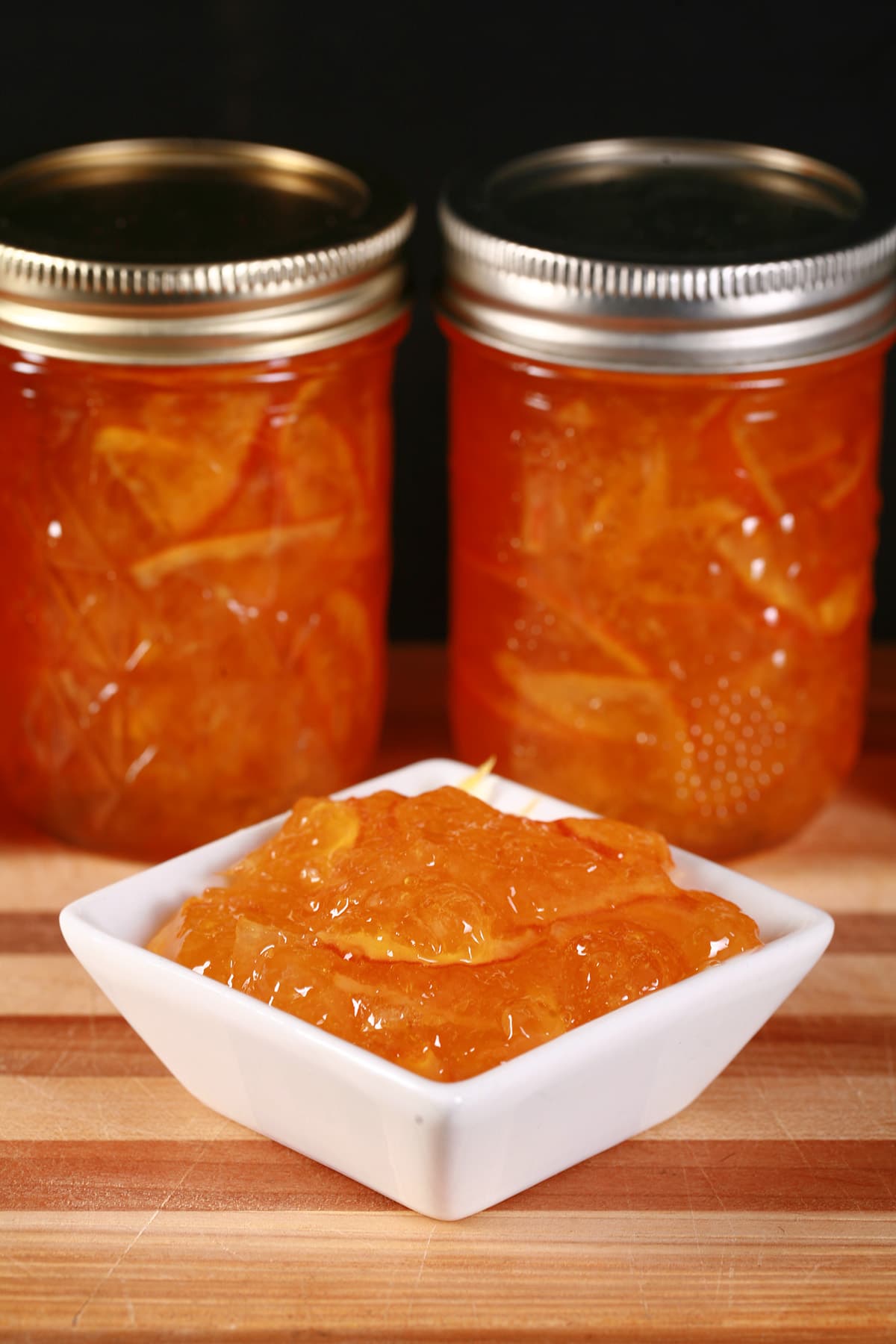A row of small jars of clementine marmalade, with a small dish of marmalade in front.