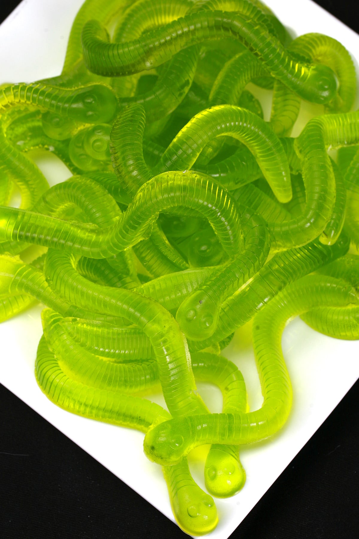 A white plate with a pile of bright green, pickle flavoured gummy worms on it.