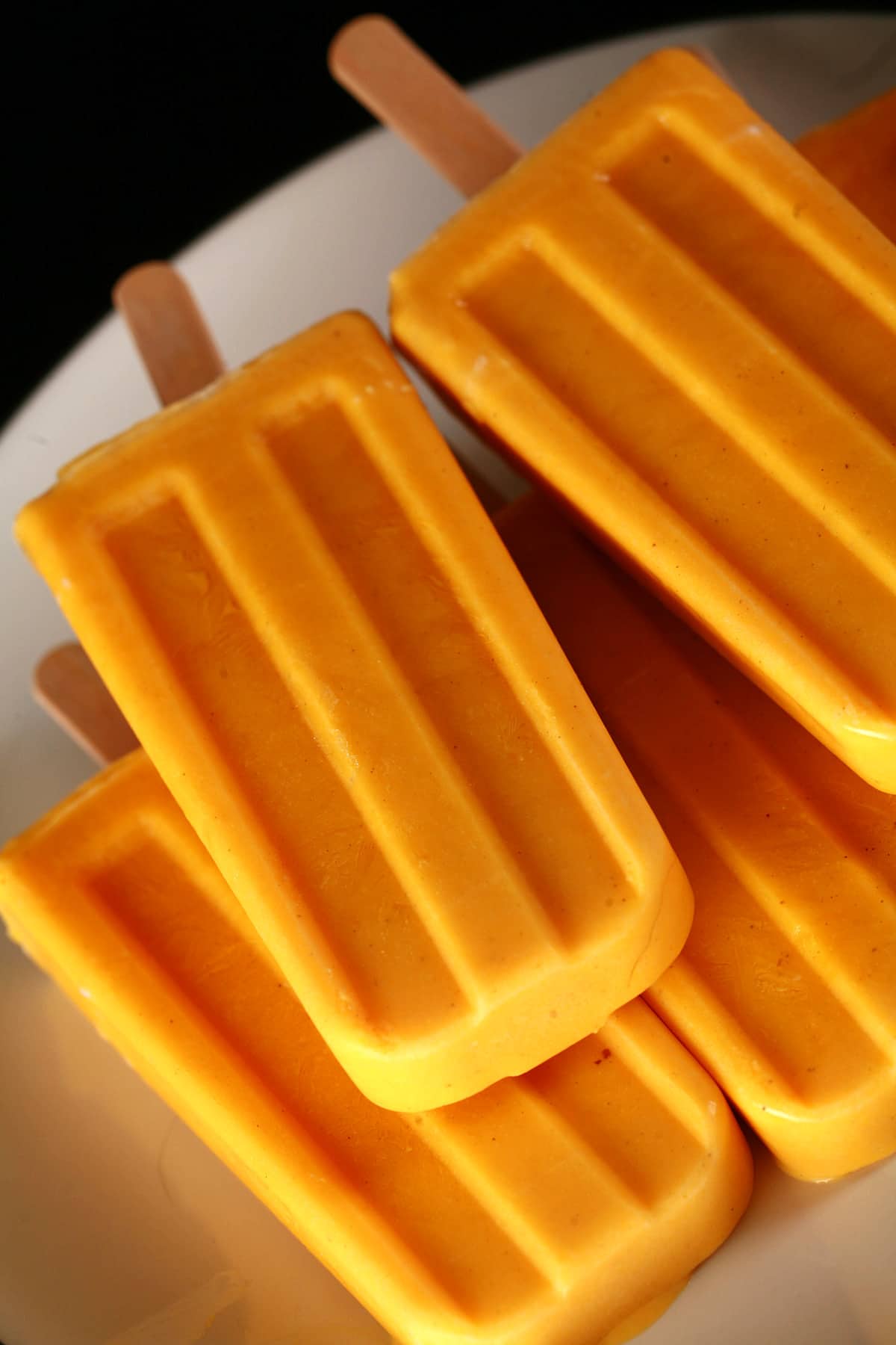 Several deep orange-yellow Mango Lassi Popsicles on a white plate.