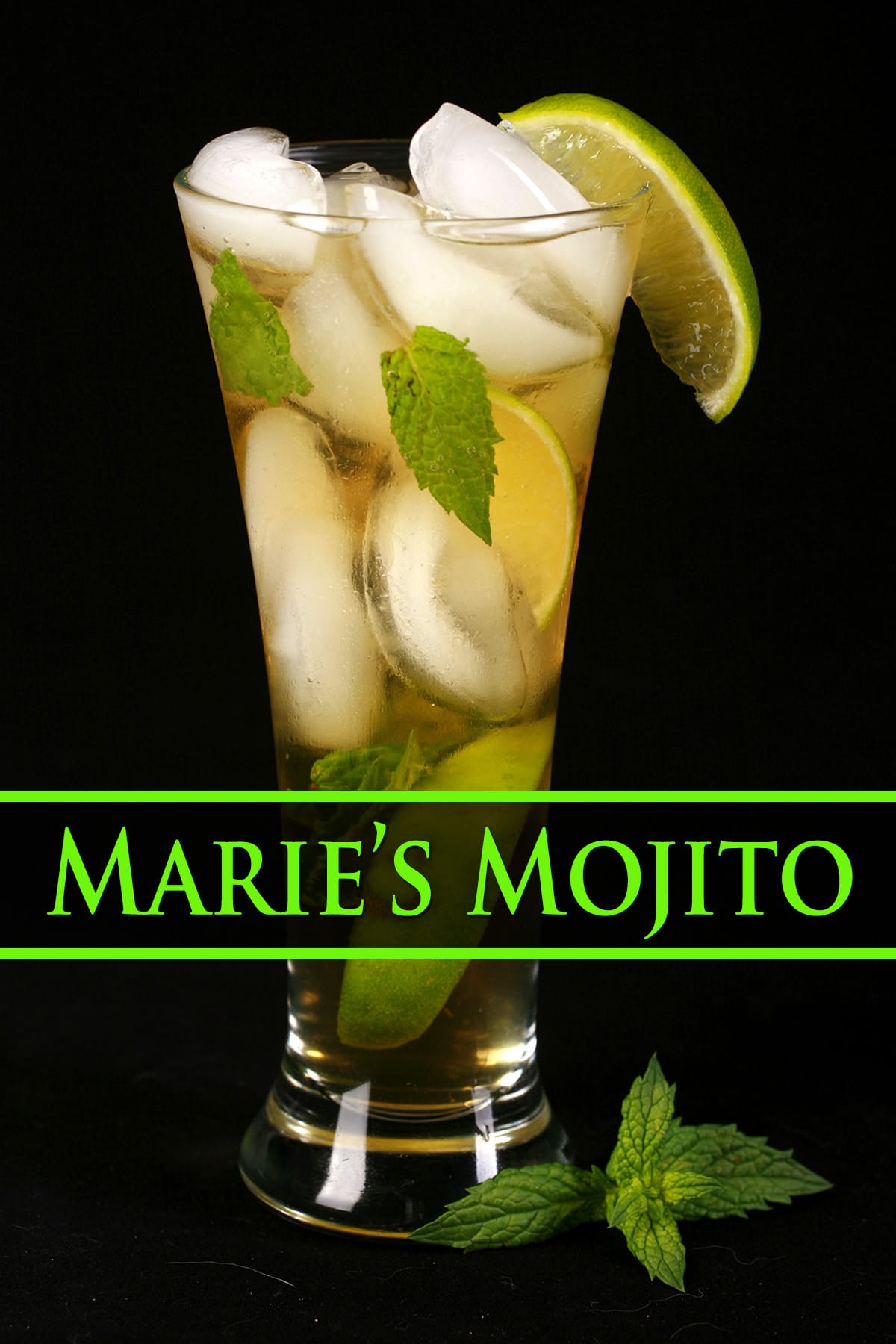 A close up view of Marie's Mojito Recipe - A tall glass with ice, limes, and mint in it, along with a pale amber liquid. It is garnished with a slice of lime.
