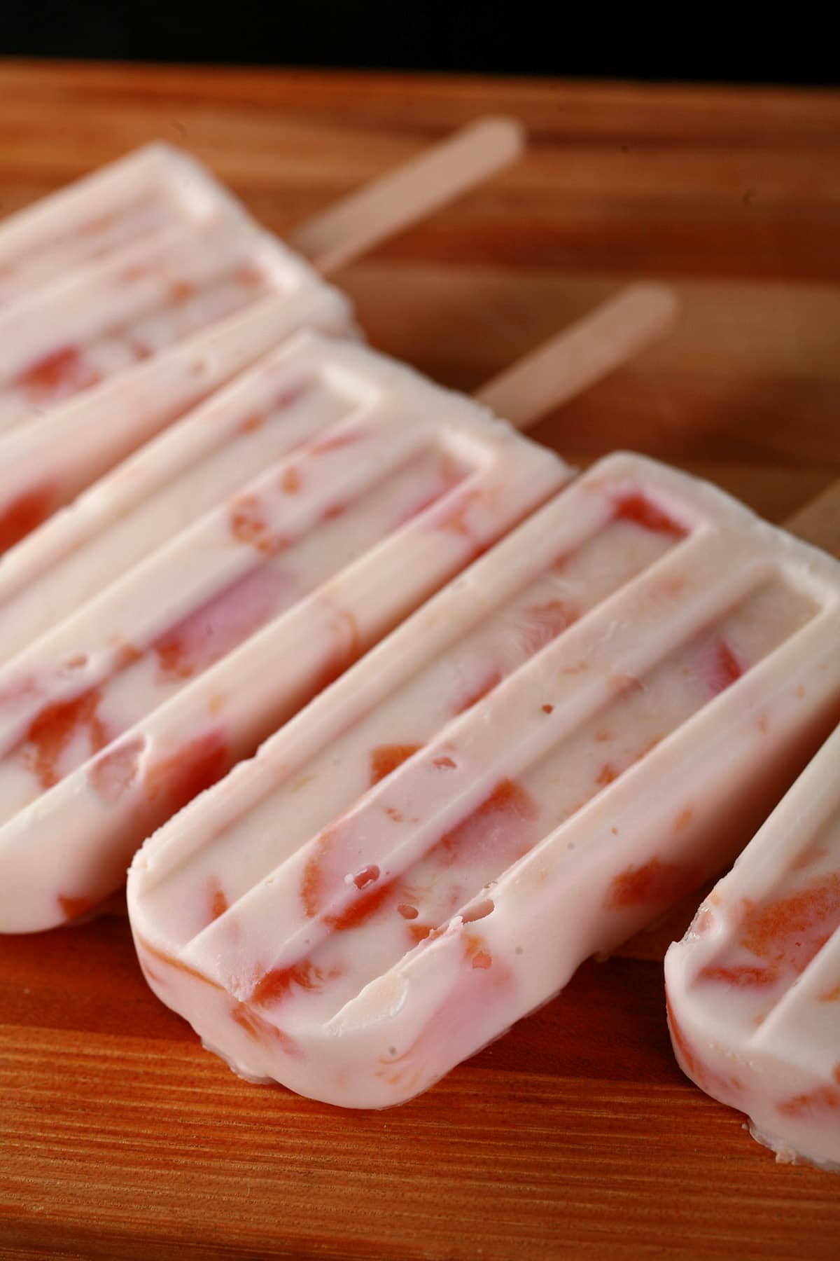 Southern Comfort Peaches N Cream Popsicles, laid out on a striped wooden cutting board.