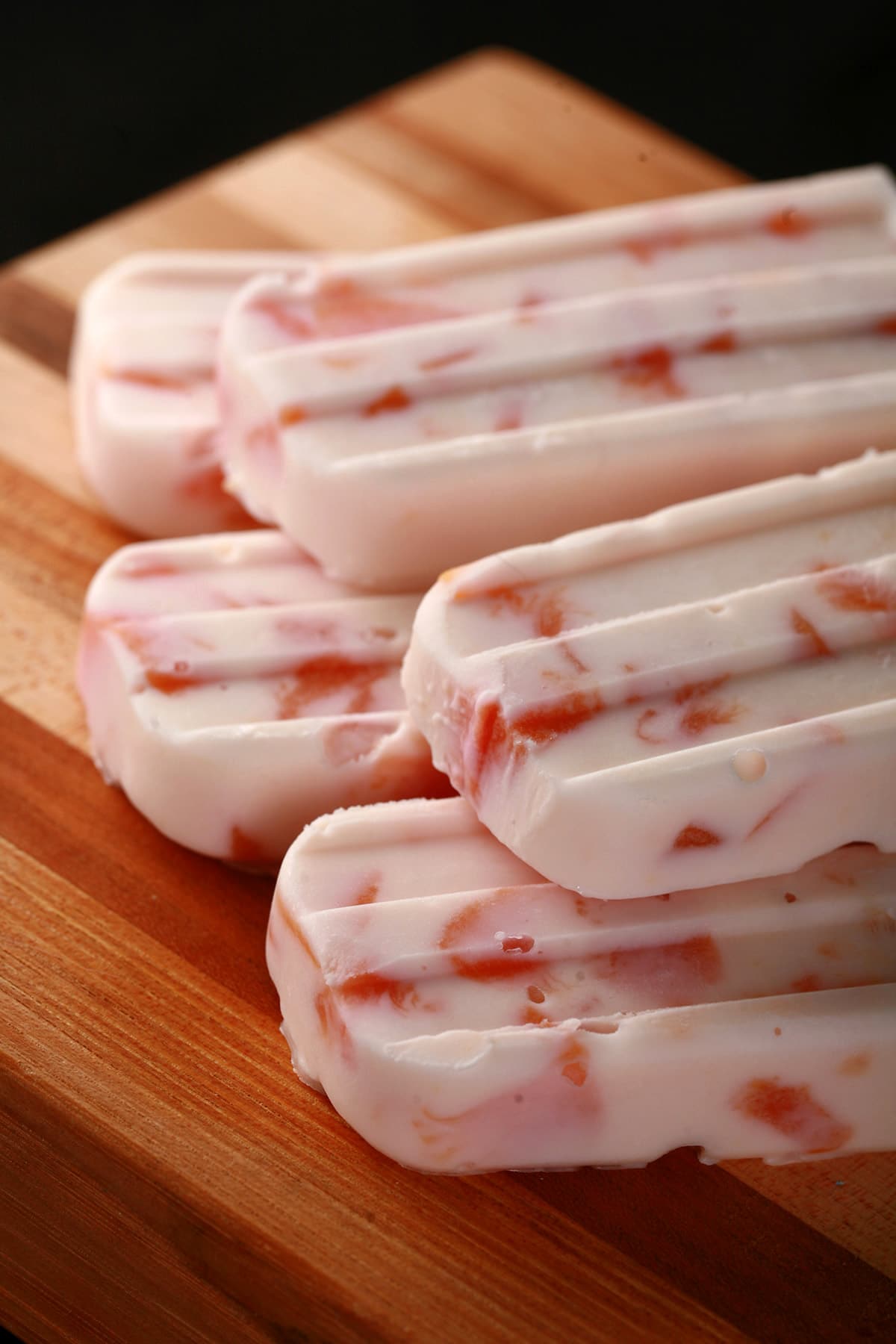 Southern Comfort Peaches N Cream Popsicles, laid out on a striped wooden cutting board.