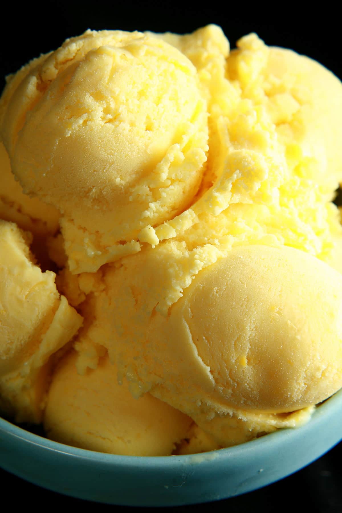 A small blue bowl, piled high with scoops of a yellow coloured sweet corn ice cream.
