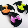 2 Black velvet cupcakes, frosted with bright icing - electric purple, lime green, and orange - and topped with a 3D pair of royal icing bat wings.