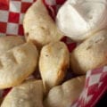 Perfectly fried perogies are mounded in a red basket, accompanied by a small bowl of sour cream.