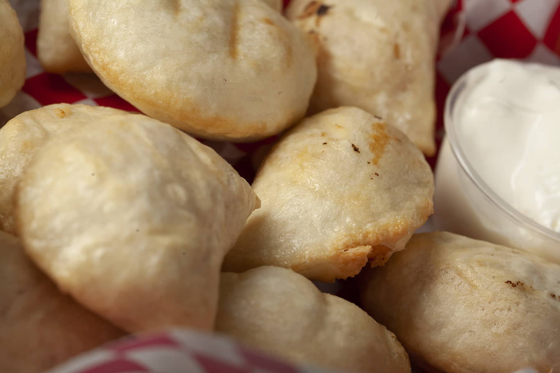Perfectly cooked perogies are mounded in a red basket, accompanied by a small bowl of sour cream.