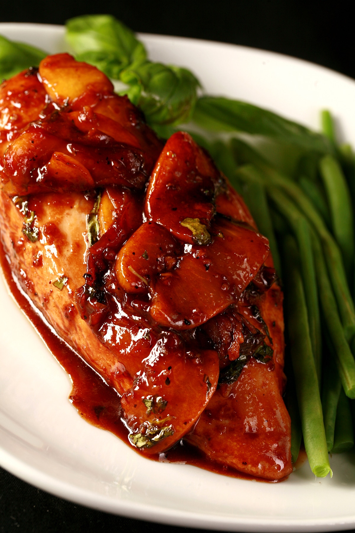Plate with one chicken breast topped with sliced peaches and a reddish-brown sauce, with green beans on the side.