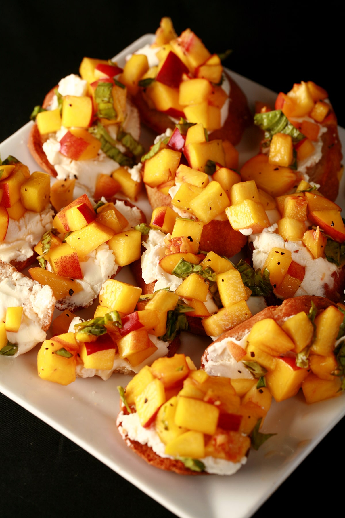 An oval plate with several servings of balsamic peach bruschetta - toasted baguette slices with goat cheese, chopped peaches, and ribbons of fresh basil.