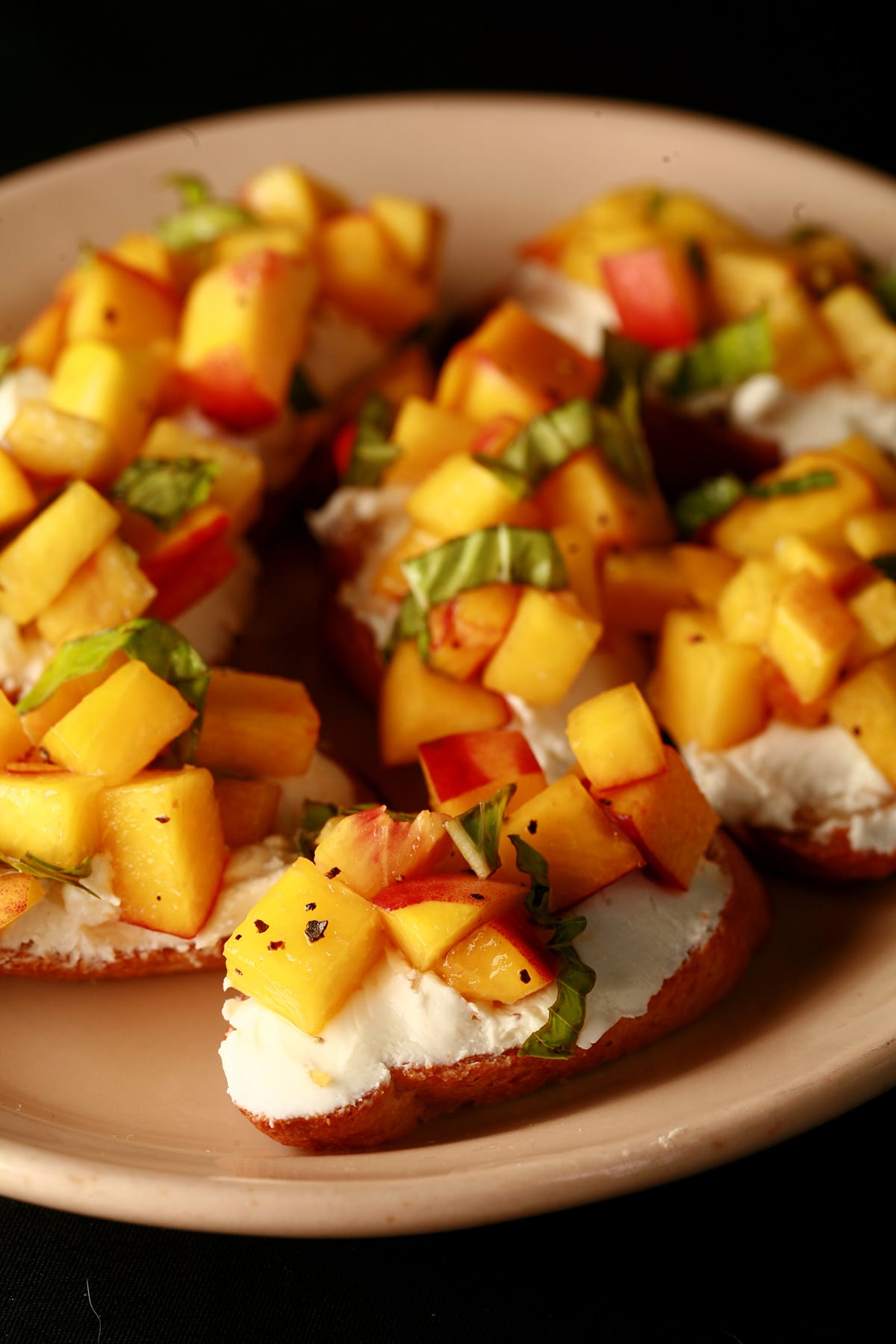 An oval plate with several servings of balsamic peach bruschetta - toasted baguette slices with goat cheese, chopped peaches, and ribbons of fresh basil.