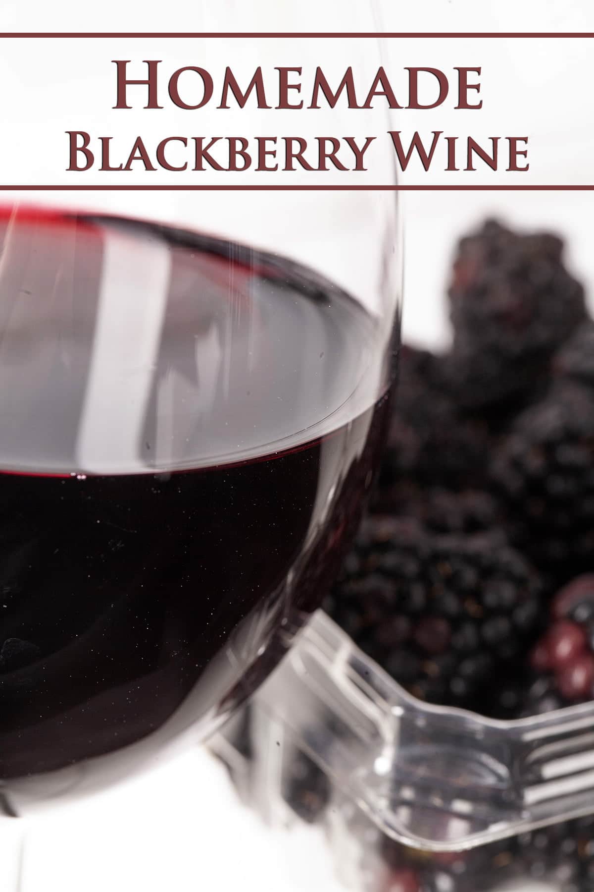 A glass of deep purple blackberry wine in front of a tray of blackberries.
