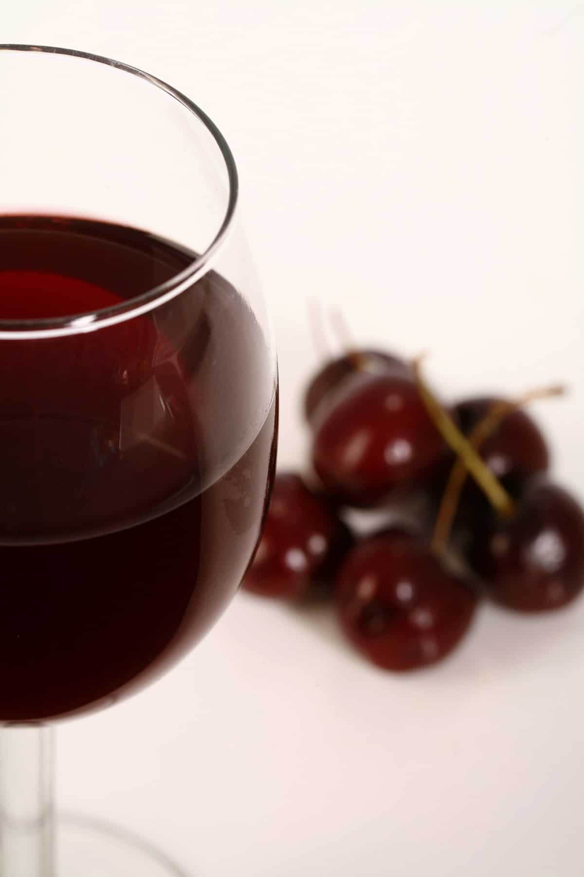 A glass of dark red cherry wine, with several cherries at the base of it.