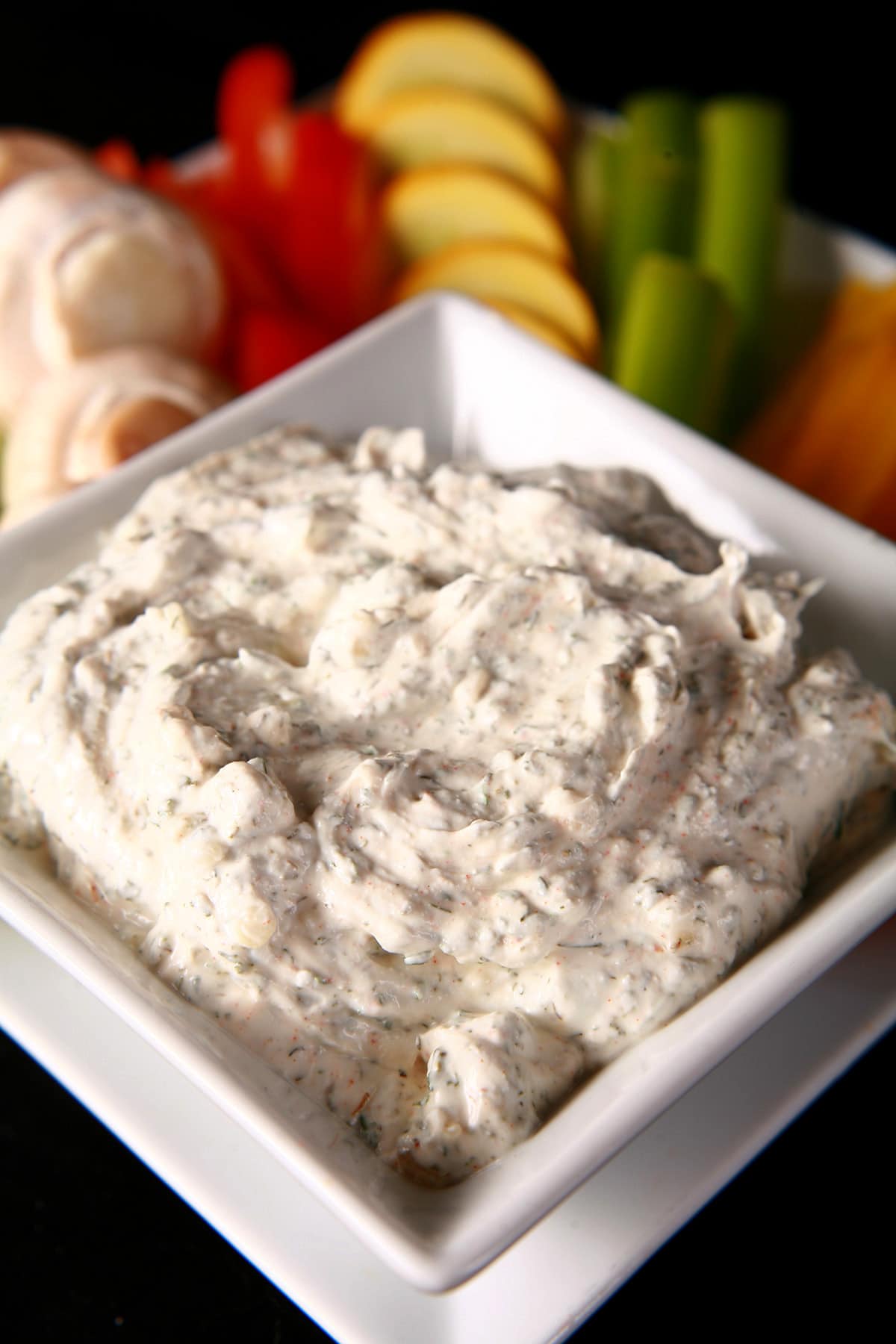 A close up view of a bowl of a thick veggie dip.  It is white with green flecks throughout.