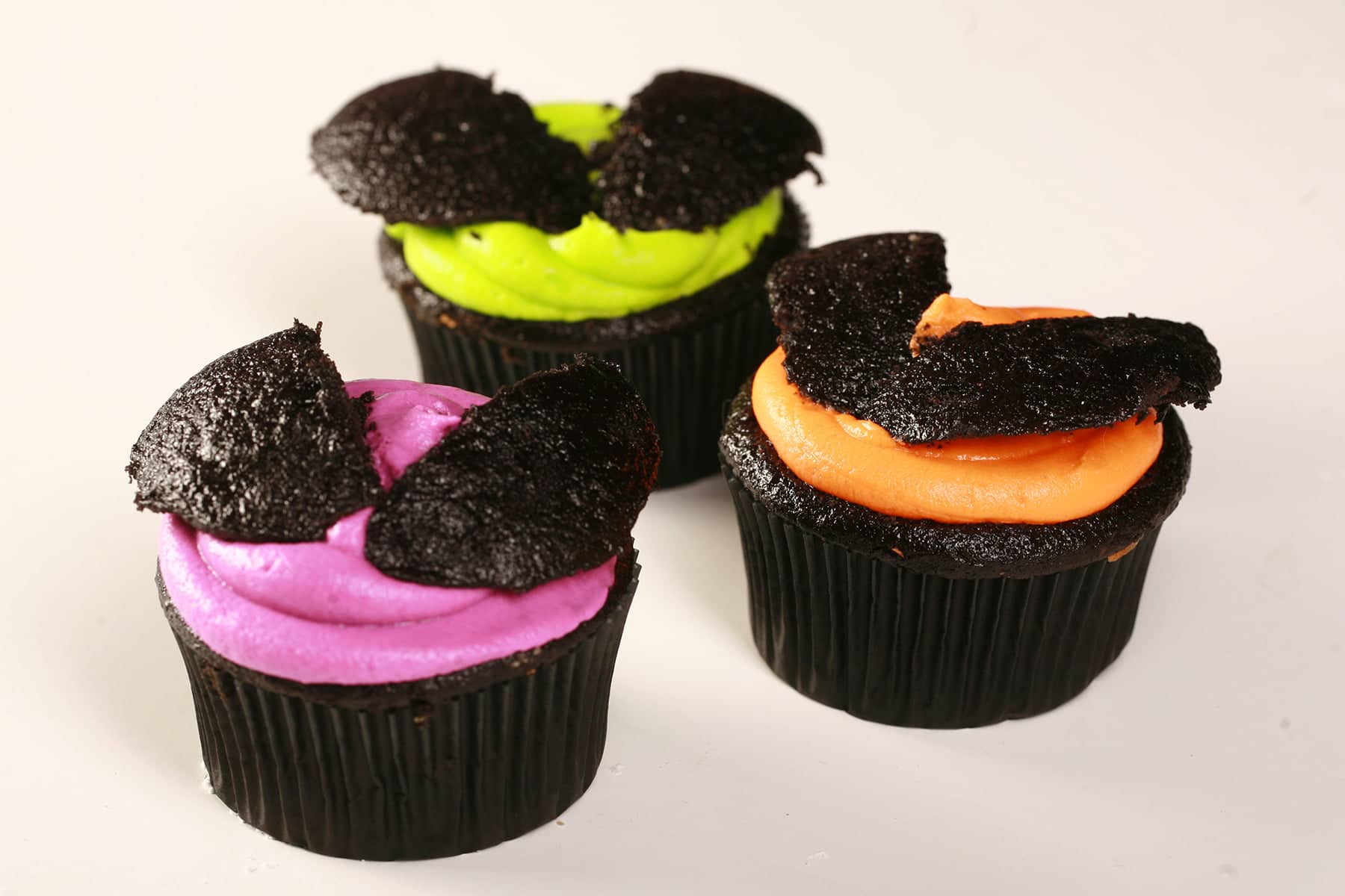 3 Easy Halloween Bat Cupcakes - Black Velvet Cupcakes with the dome cut off, frosted with brightly coloured icing - electric purple, lime green, and orange - then the halved dome of the cupcake is re-positioned on top to form bat wings.