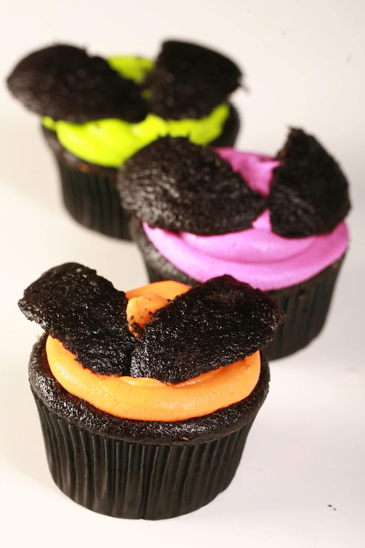 3 Easy Halloween Bat Cupcakes - Black Velvet Cupcakes with the dome cut off, frosted with brightly coloured icing - electric purple, lime green, and orange - then the halved dome of the cupcake is re-positioned on top to form bat wings.
