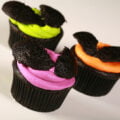 3 Easy halloween Bat Cupcakes - Black Velvet Cupcakes with the dome cut off, frosted with brightly coloured icing - electric purple, lime green, and orange - then the halved dome of the cupcake is re-positioned on top to form bat wings.