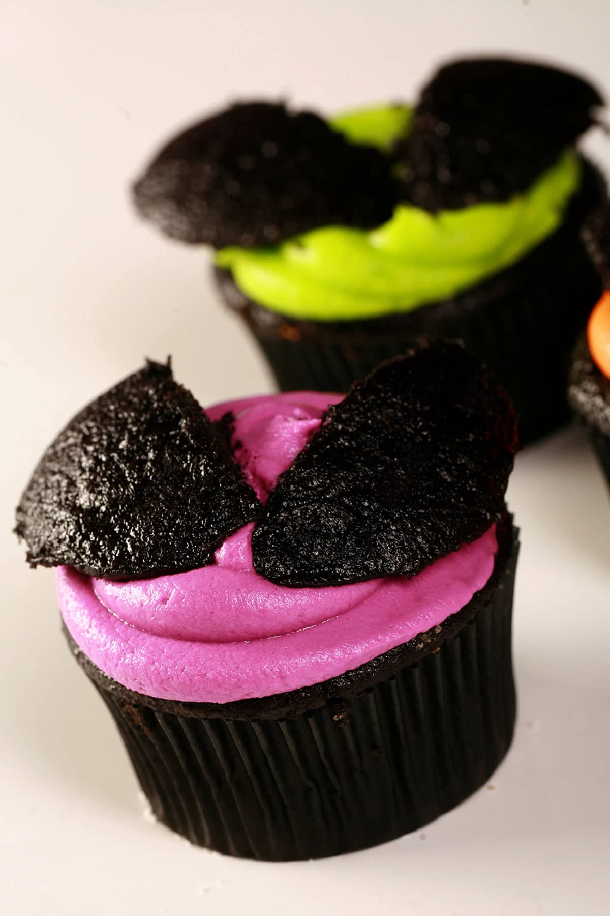 3 Easy Halloween Bat Cupcakes - Black Velvet Cupcakes with the dome cut off, frosted with brightly coloured icing - electric purple, lime green, and orange - then the halved dome of the cupcake is re-positioned on top to form bat wings.