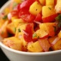 A close up photo of fresh peach salsa, with peaches, red pepper, red onions, jamapeno, and cilatro visible.
