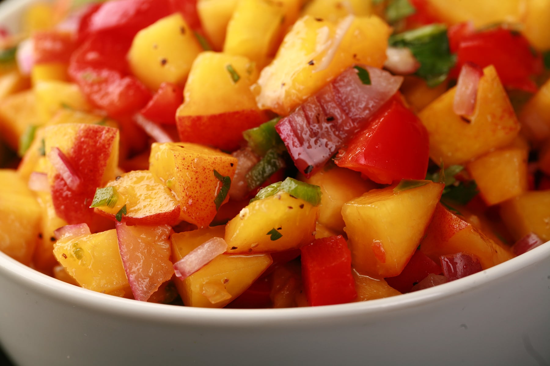 A close up photo of fresh peach salsa, with peaches, red pepper, red onions, jamapeno, and cilatro visible.
