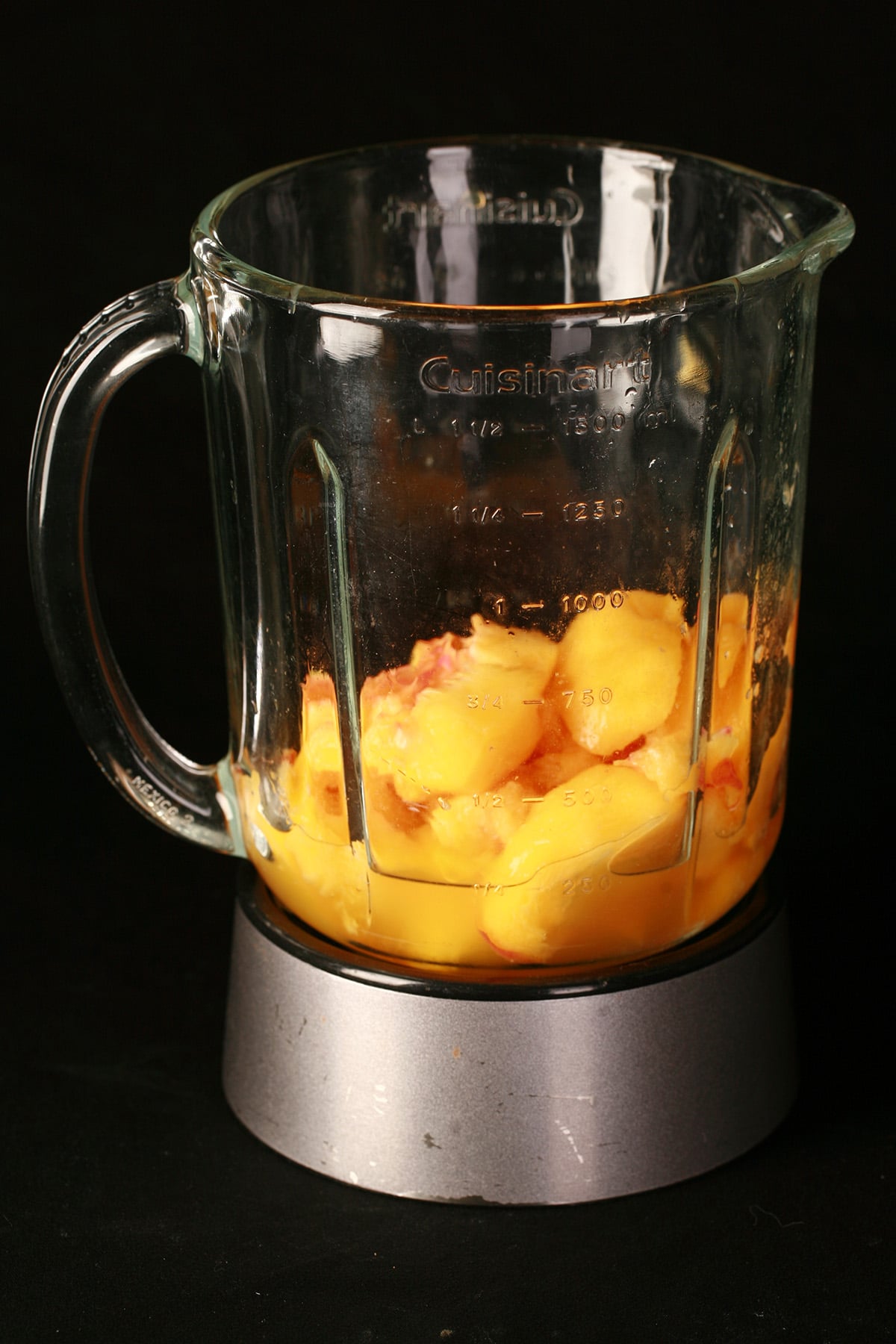 A blender with peach chunks in it, against a black background.