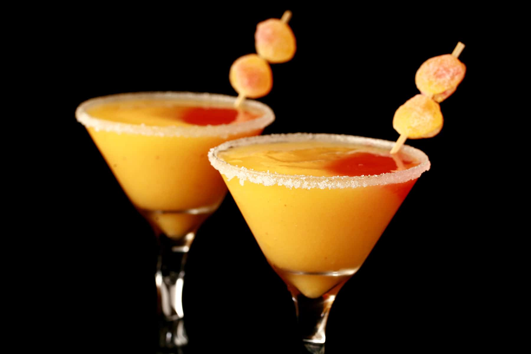 Two martini cocktail glasses with fuzzy peach candy cocktail - a peach coloured slush with a round section of red slush in it, garnished with gummy candies.