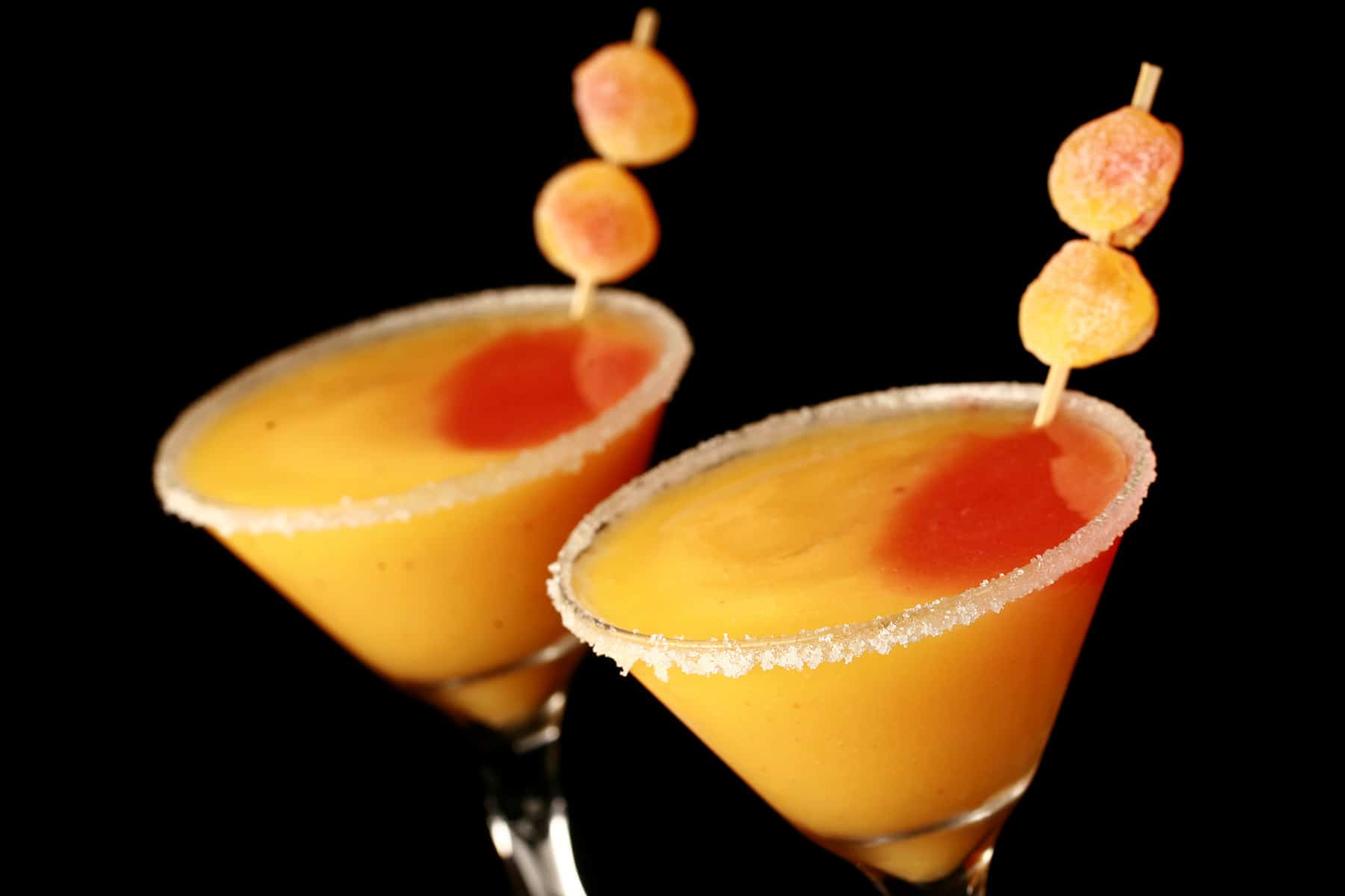 Two martini cocktail glasses with fuzzy peach candy cocktail - a peach coloured slush with a round section of red slush in it, garnished with gummy candies.