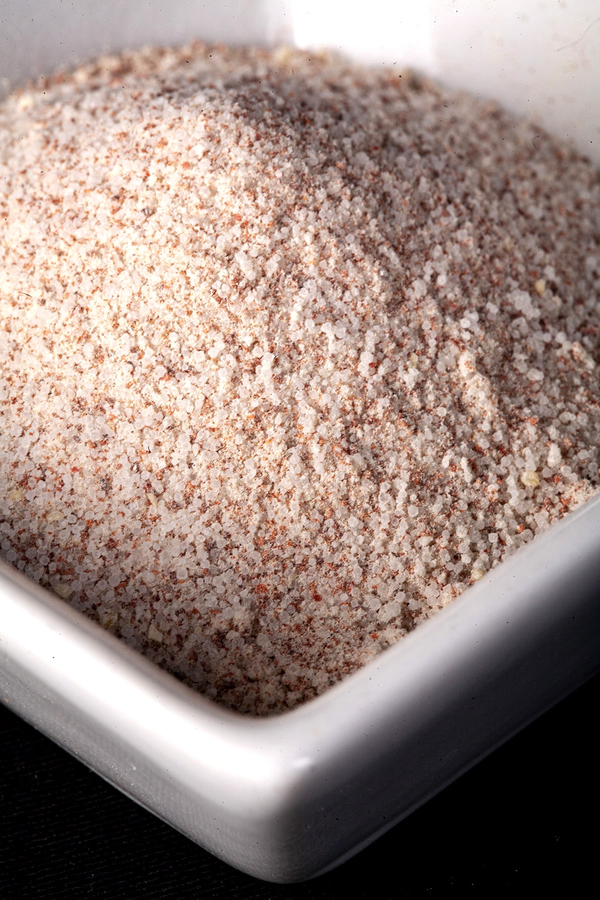 A small, square shaped white bowl with a pinkish seasoning salt mixture in it.