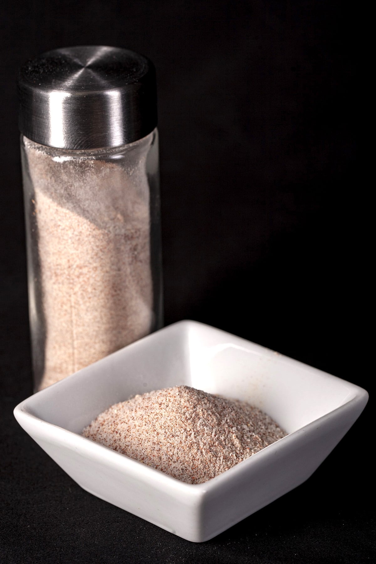 A small, square shaped white bowl with a pinkish seasoning salt mixture in it.