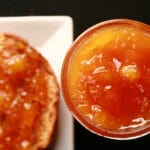 Close up photo of a small jar of orange coloured jam next to a piece of toast