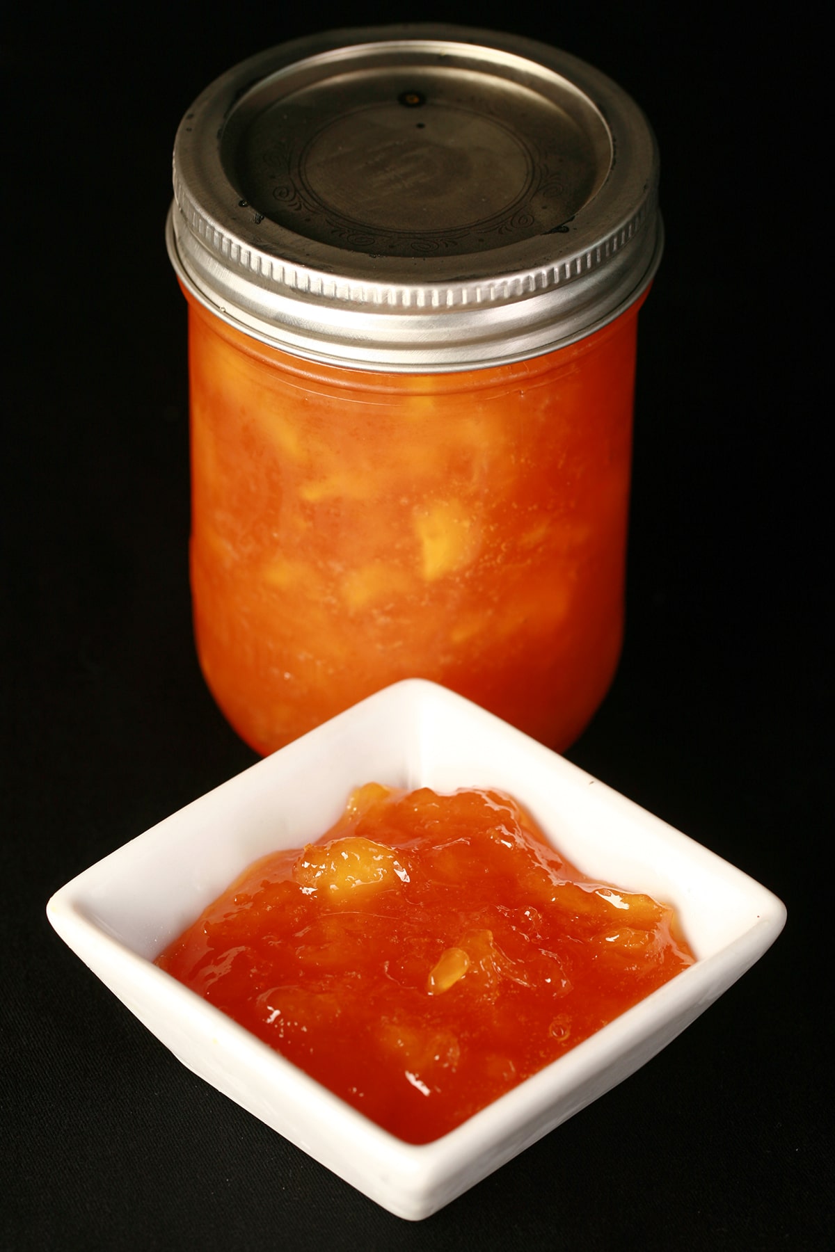 A jar of chunky peach jam, next to a small bowl of the jam.