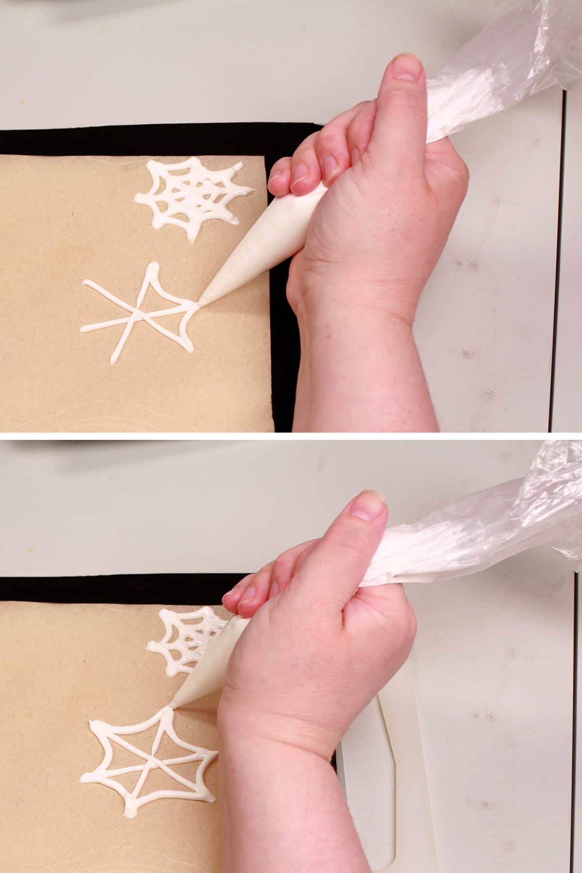 A hand uses a pastry bag full of white royal icing to pipe spider webs on a parchment lined baking sheet.