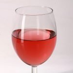 A glass of pale red homemade strawberry wine.