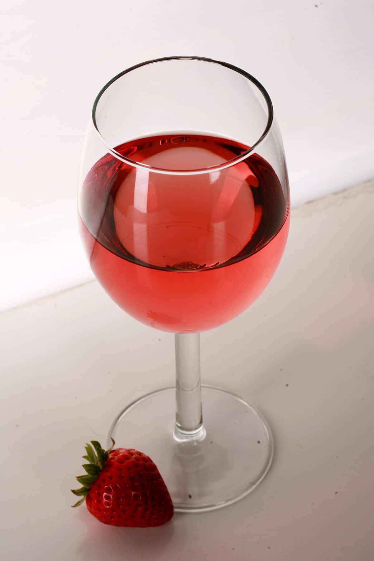 A glass of pale red strawberry wine with a single strawberry at the base of the glass.
