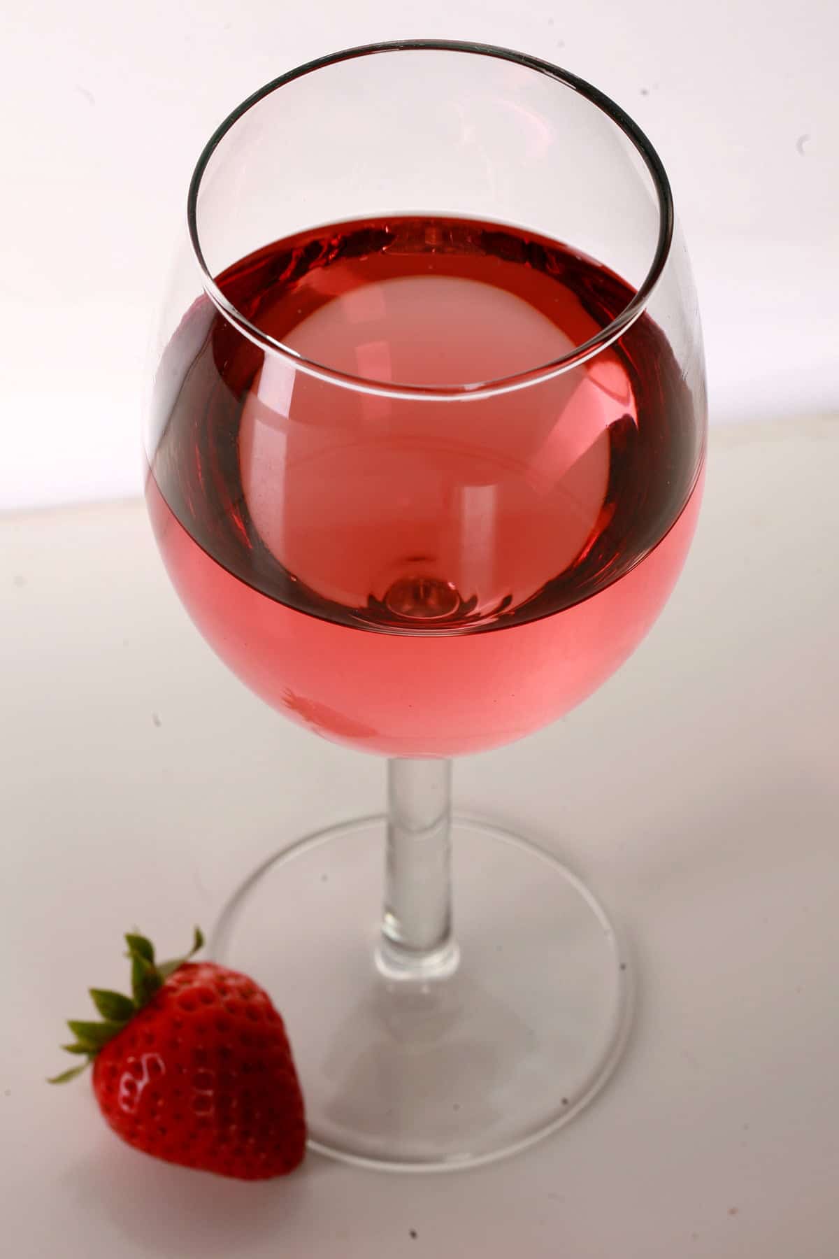 A glass of pale red strawberry wine with a single strawberry at the base of the glass.