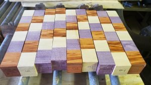 Several strips of wood, comprised of smaller cubes, are seen on a table. Each strip has been sanded to have flat sides.